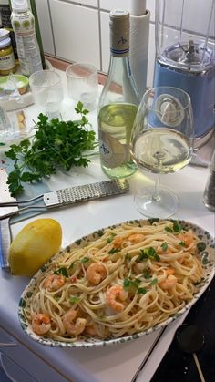 a plate of pasta with shrimp and parsley next to some lemons, wine glasses and bottles