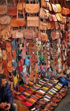 a man sitting in front of a store filled with lots of handbags and purses