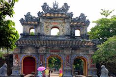 two women with umbrellas are standing in front of an old building that has statues on it