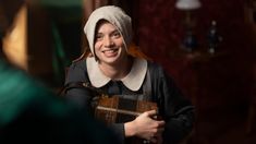 a woman in a bonnet smiles while holding an instrument