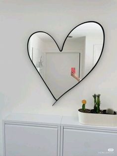 a heart shaped mirror hanging on the wall next to a white cabinet and potted plant