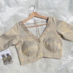 Elevate your traditional wardrobe with this stunning light beige golden sequin blouse, designed for elegance and comfort. Crafted from luxurious sequin fabric, this blouse features a stylish V-neck on both the front and back, perfect for adding a touch of sophistication to your ensemble. The back thread detailing adds a unique flair, while the lace trim around the neckline enhances its delicate beauty. Ideal for pairing with sarees or lehengas, this versatile piece will make you stand out at wed Cheap Gold Blouse With Cutdana, V-neck Blouse Piece For Diwali Reception, Elegant V-neck Lehenga With Zari Work, Festive V-neck Choli With Mirror Work, Elegant V-neck Lehenga With Resham Embroidery, Elegant V-neck Choli With Resham Embroidery, Elegant Lehenga With Resham Embroidery And V-neck, Elegant V-neck Blouse For Festive Occasions, Elegant Festive V-neck Blouse