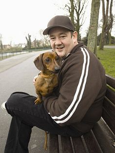 a man sitting on a bench holding a small dog