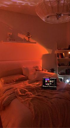 a laptop computer sitting on top of a bed in a room with orange light coming from the ceiling