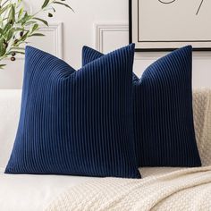 two blue pillows sitting on top of a white couch next to a potted plant