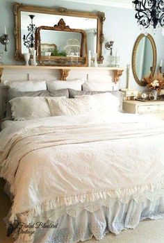 a white bed sitting in a bedroom next to a chandelier and two mirrors