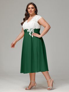 a woman wearing a green dress with white flowers on the waist and sleeves, standing in front of a gray background