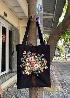 a black bag hanging from a tree with pink and white flowers on it's side