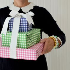 a woman holding three wrapped presents in different colors and patterns, both with white ribbons