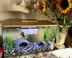 a fish tank sitting on top of a table next to a vase filled with flowers