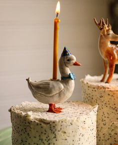 two cakes decorated with frosting and animal figurines, one has a candle in the shape of a duck