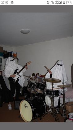 two people in white costumes playing drums and singing into microphones while another person dressed as ghost behind them plays guitar