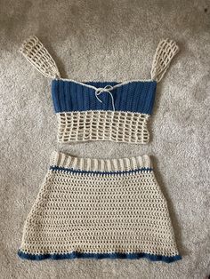 two pieces of crocheted clothing laying on the floor, one with blue and white stripes