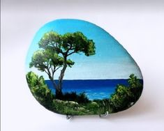 there is a painted rock with trees and the ocean in the backgroung