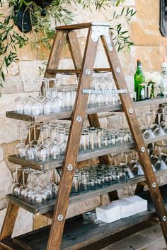 a wooden shelf filled with lots of glasses on top of a table next to a wall