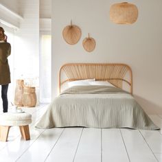 a woman standing in front of a bed with wicker headboard