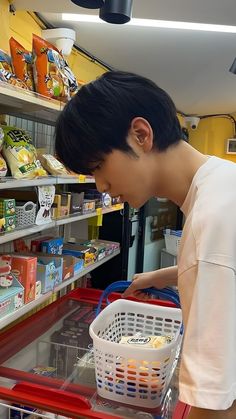 a young man is looking at food in a shopping basket while standing next to a shelf