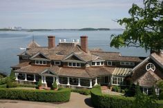 a large house sitting on top of a lush green hillside next to the ocean with lots of windows