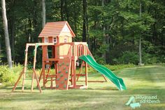 a wooden play set with a green slide and climbing frame in the foreground, surrounded by trees