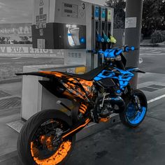 a black and orange motorcycle parked at a gas station with blue flames painted on it