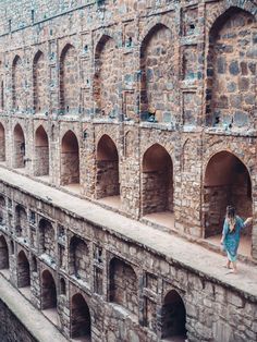 a woman standing on the side of an old brick building with arches and doorways