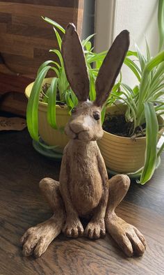 a statue of a rabbit sitting on top of a wooden table next to potted plants