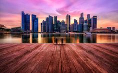 an empty wooden deck overlooks a cityscape at sunset, with boats in the water