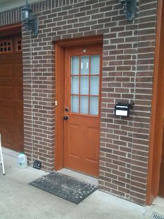 a brick building with two brown doors and a black door mat on the sidewalk next to it