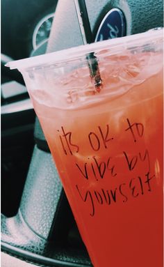 a drink in a plastic cup sitting on top of a car steering wheel with the words it's ok to vibe by yourself