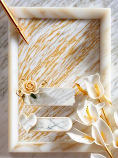 a white and gold frame with some flowers on it next to a pen, pencil and paper