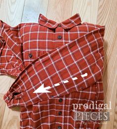 a red and white checkered shirt laying on top of a wooden floor next to a pair of scissors