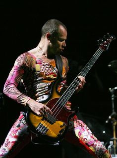 a man with tattoos on his body playing a bass guitar in front of a microphone