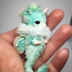 a hand is holding a small green and white doll with horns on it's head