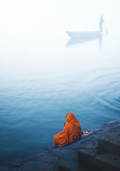 a person sitting on the edge of a body of water with a boat in the background