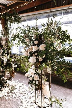 an arrangement of white flowers and greenery on display in front of a window at a wedding