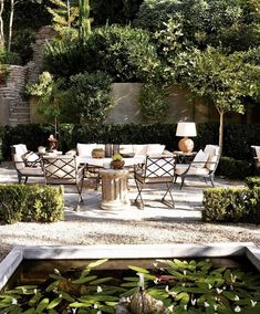 an outdoor dining area with chairs, tables and water feature in the center surrounded by greenery