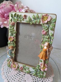 a small photo frame with a fairy on it next to pink flowers and a lace doily