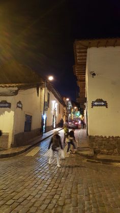 three people walking down a cobblestone street at night