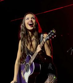 a woman singing into a microphone while holding a guitar