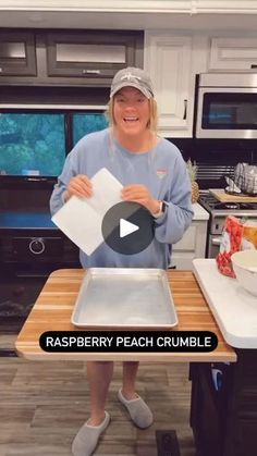 a woman standing in front of a counter holding a piece of paper with the words raspberry peach crumble on it