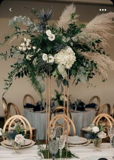 a tall vase filled with flowers and greenery on top of a table