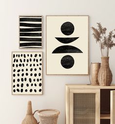 three black and white art pieces hanging on the wall next to a vase with flowers in it