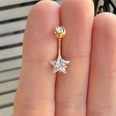 a person's hand holding a gold nose ring with a star shaped diamond