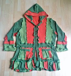 a green and red coat with ruffles on the hood sitting on a wooden floor