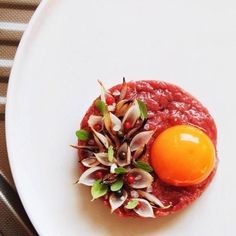 a white plate topped with meat and an egg on top of it next to a fork