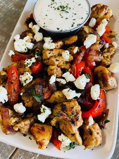 a white plate topped with chicken and veggies next to a bowl of ranch dressing