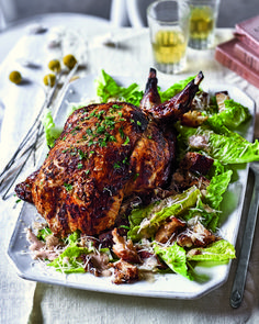 a white plate topped with a chicken and lettuce covered in sauce next to silverware