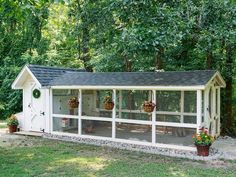 a white chicken coop in the middle of a yard with potted plants on it