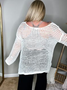 a woman standing in front of a mirror wearing black pants and a white sweater with holes on it