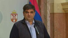 a man standing at a podium with a microphone in front of him and flags behind him